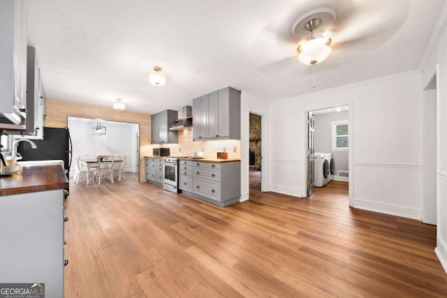 kitchen featuring washing machine and dryer, stainless steel range, gray cabinetry, and wall chimney exhaust hood