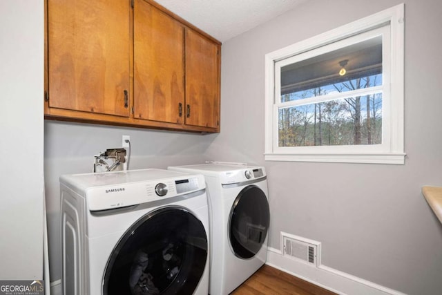 laundry room with cabinets, washing machine and dryer, wood-type flooring, and a textured ceiling