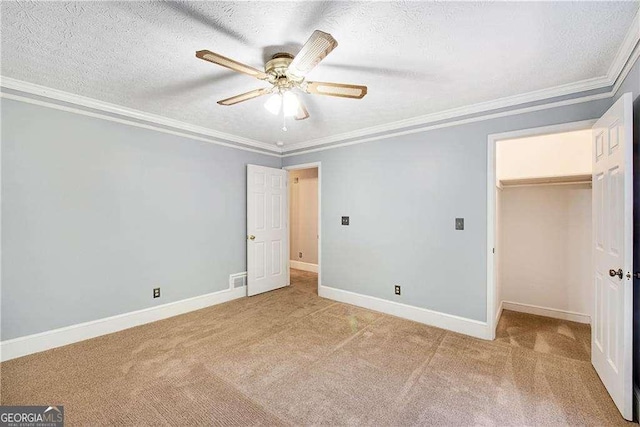 unfurnished bedroom with a closet, a spacious closet, a textured ceiling, crown molding, and light carpet