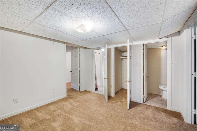 unfurnished bedroom featuring a drop ceiling, ensuite bath, and light carpet