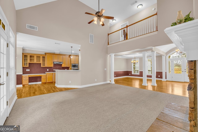 unfurnished living room with ceiling fan with notable chandelier, light wood-type flooring, ornate columns, and high vaulted ceiling