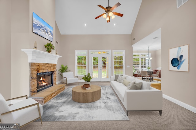 carpeted living room with ceiling fan, a stone fireplace, high vaulted ceiling, and french doors