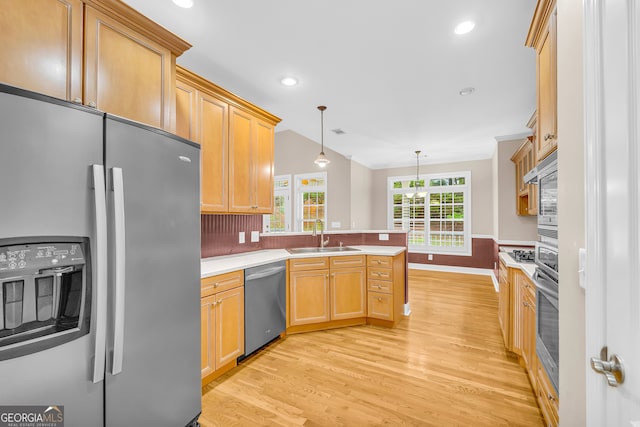 kitchen with light brown cabinets, sink, light wood-type flooring, decorative light fixtures, and stainless steel appliances