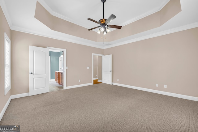 unfurnished bedroom featuring light carpet, ensuite bathroom, a tray ceiling, ceiling fan, and crown molding