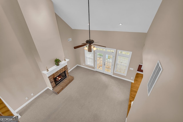 carpeted living room featuring ceiling fan, a fireplace, high vaulted ceiling, and french doors