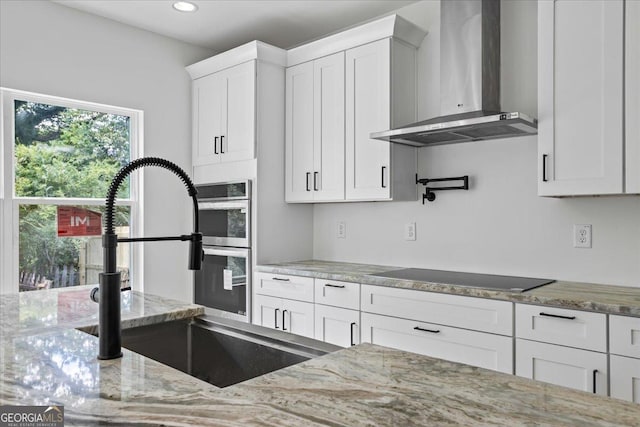 kitchen with sink, white cabinets, light stone countertops, black electric cooktop, and wall chimney exhaust hood