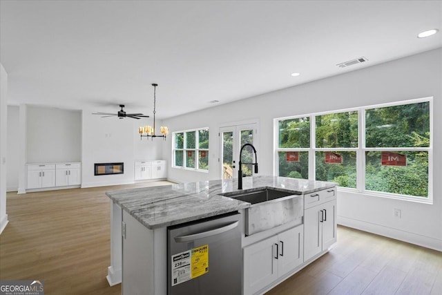 kitchen featuring sink, light stone counters, a center island with sink, dishwashing machine, and white cabinets