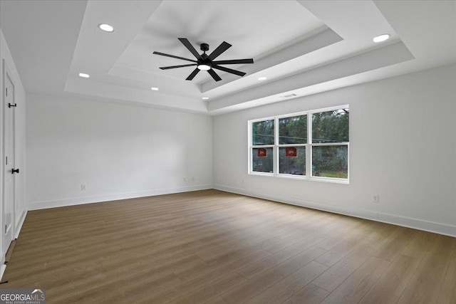 empty room with a tray ceiling, ceiling fan, and hardwood / wood-style flooring