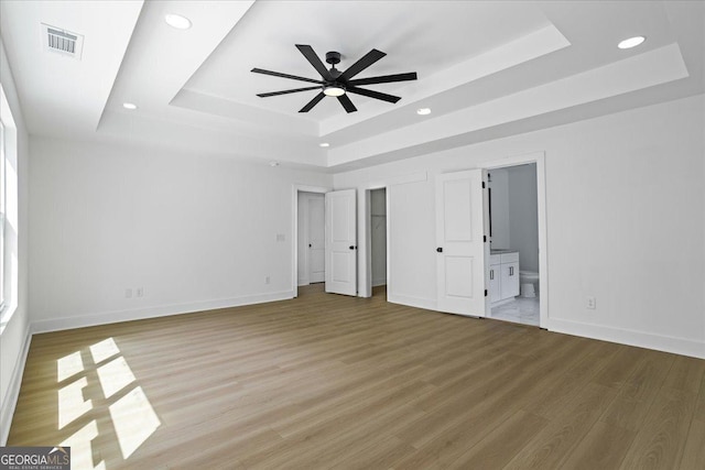 unfurnished bedroom with ceiling fan, ensuite bath, a raised ceiling, and hardwood / wood-style flooring