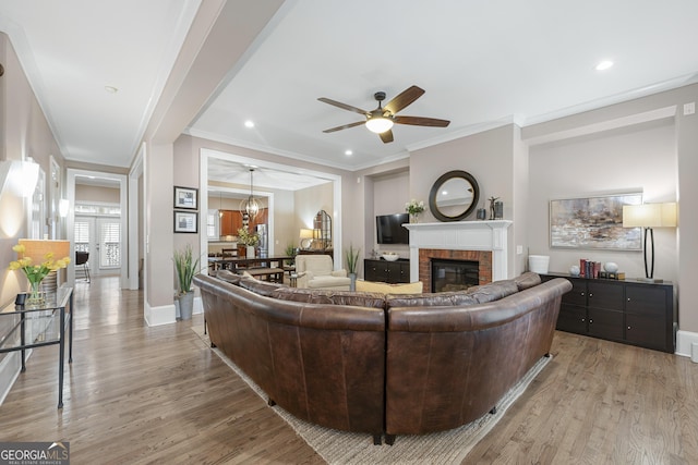 living room with a fireplace, light wood-type flooring, ceiling fan, and crown molding