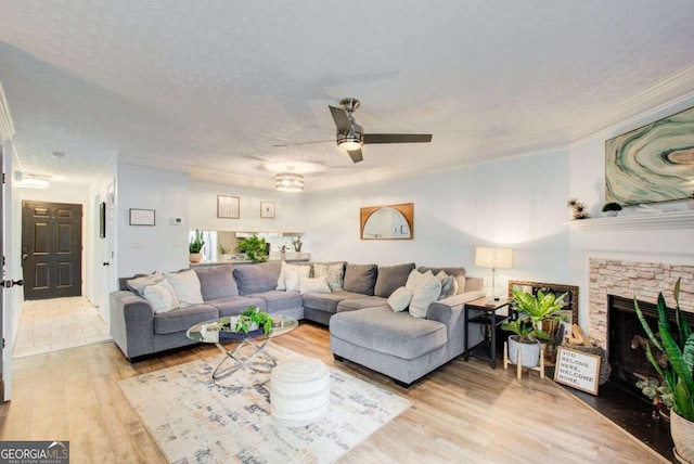 living room with a textured ceiling, ceiling fan, crown molding, wood-type flooring, and a fireplace