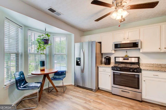 kitchen with white cabinets, ceiling fan, light hardwood / wood-style floors, light stone counters, and stainless steel appliances