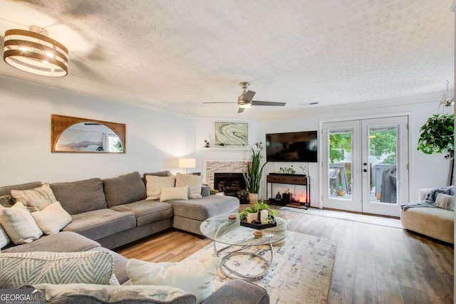 living room with french doors, wood-type flooring, a textured ceiling, a fireplace, and ceiling fan with notable chandelier