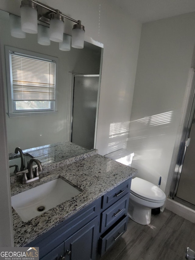 bathroom featuring wood-type flooring, vanity, toilet, and a shower with door