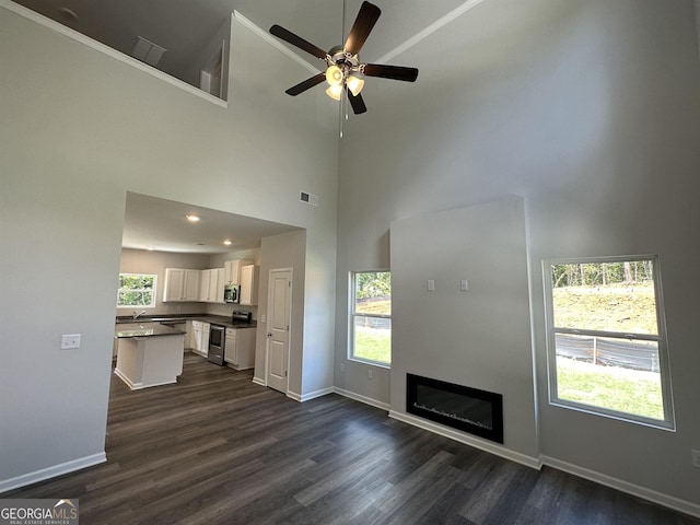 unfurnished living room with ceiling fan, dark hardwood / wood-style flooring, sink, and a high ceiling