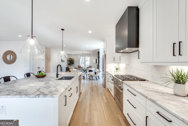 kitchen featuring wall chimney exhaust hood, sink, white cabinets, hanging light fixtures, and a large island