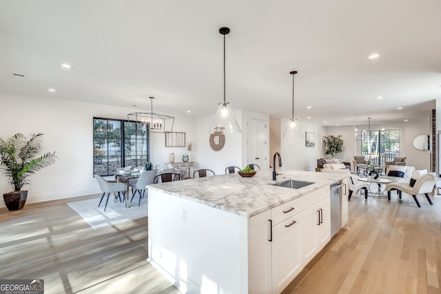 kitchen with sink, decorative light fixtures, white cabinetry, and an island with sink