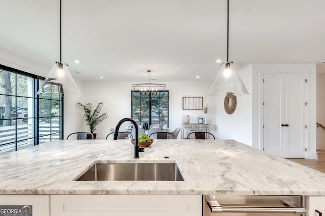 kitchen featuring light stone counters, decorative light fixtures, light hardwood / wood-style flooring, and sink