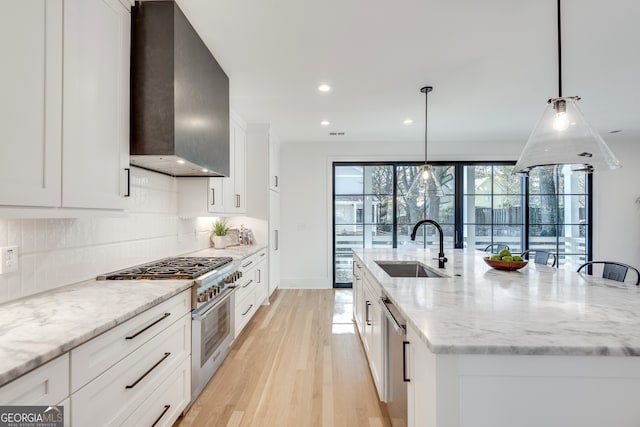 kitchen with sink, wall chimney exhaust hood, an island with sink, and decorative light fixtures