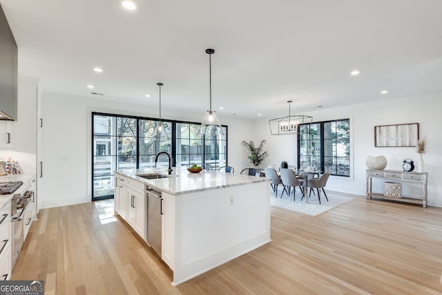 kitchen with light stone countertops, sink, a center island with sink, white cabinets, and light wood-type flooring