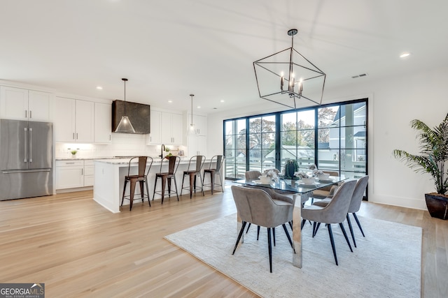 dining space featuring sink, a chandelier, and light wood-type flooring