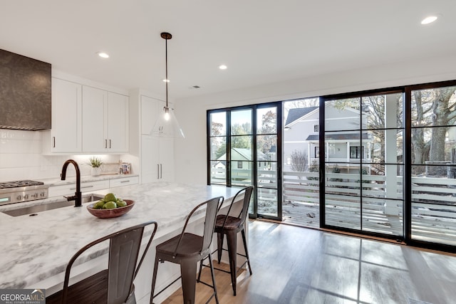 kitchen featuring sink, light stone counters, backsplash, decorative light fixtures, and white cabinets