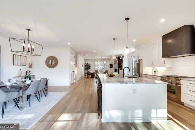 kitchen with light wood-type flooring, premium appliances, a spacious island, white cabinetry, and range hood