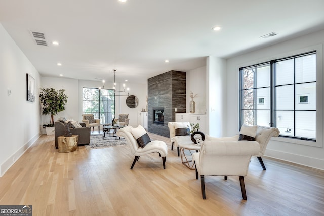 living room featuring a tiled fireplace, a chandelier, a healthy amount of sunlight, and light hardwood / wood-style floors