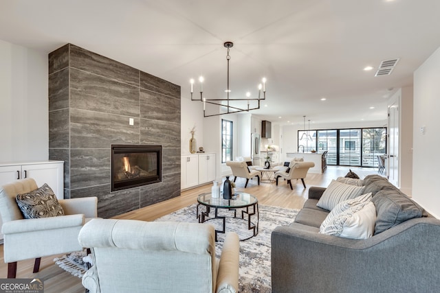 living room with a tile fireplace, light hardwood / wood-style flooring, tile walls, and a notable chandelier