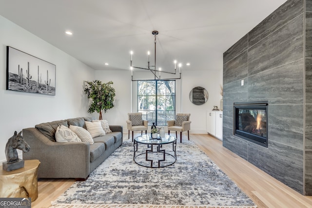 living room featuring a tiled fireplace, a chandelier, and light hardwood / wood-style floors