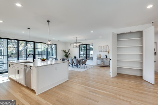 kitchen with light hardwood / wood-style floors, light stone counters, sink, and a kitchen island with sink