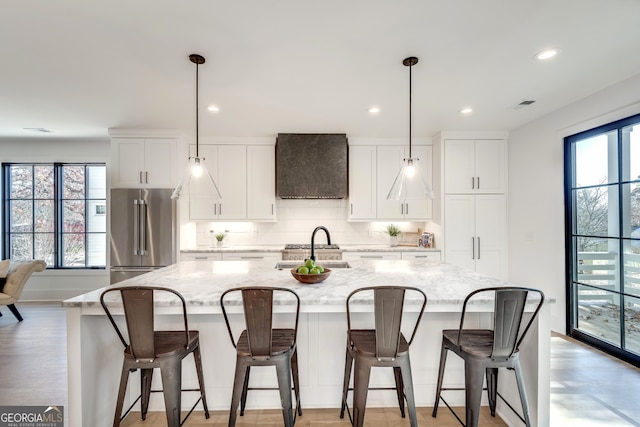 kitchen with light stone countertops, high quality fridge, a large island with sink, white cabinetry, and a breakfast bar area