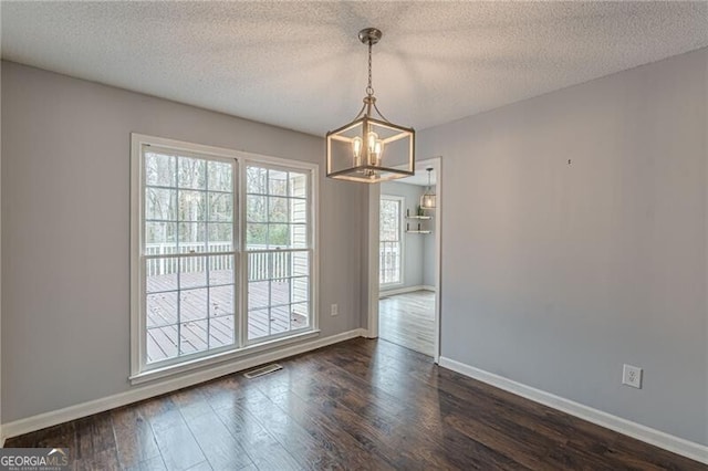 unfurnished dining area featuring dark hardwood / wood-style floors, a textured ceiling, and a chandelier