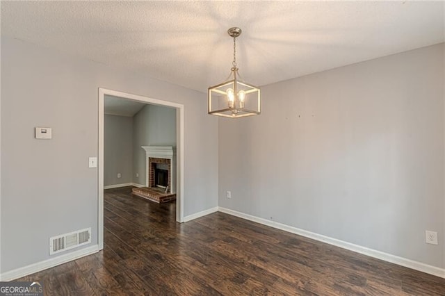 empty room with a notable chandelier, dark hardwood / wood-style flooring, a textured ceiling, and a brick fireplace