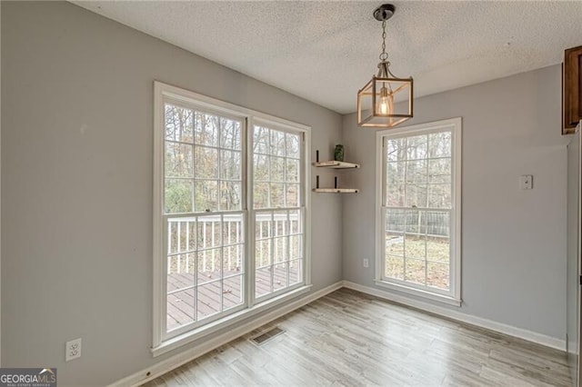 unfurnished dining area featuring light hardwood / wood-style floors, a textured ceiling, and an inviting chandelier