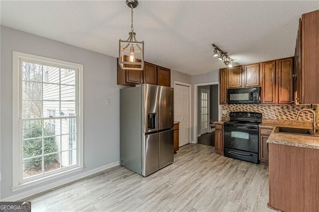 kitchen with black appliances, sink, light wood-type flooring, a textured ceiling, and decorative light fixtures