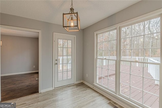 doorway to outside with light hardwood / wood-style flooring, a healthy amount of sunlight, and a textured ceiling