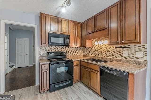 kitchen with decorative backsplash, a textured ceiling, sink, black appliances, and light hardwood / wood-style flooring