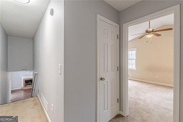 hall featuring a textured ceiling, light carpet, and lofted ceiling