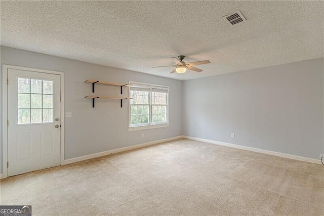 unfurnished room featuring light colored carpet, a textured ceiling, and a wealth of natural light