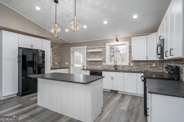 kitchen featuring wood finished floors, dark countertops, a sink, black appliances, and backsplash