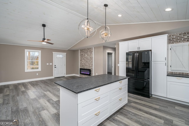 kitchen with lofted ceiling, black refrigerator, hanging light fixtures, a brick fireplace, and white cabinetry