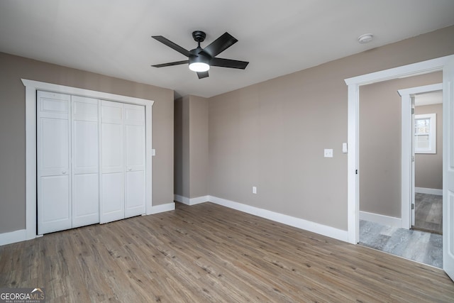 unfurnished bedroom featuring baseboards, wood finished floors, a closet, and a ceiling fan