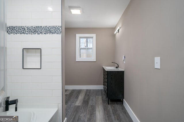 full bath with vanity, a bathtub, baseboards, and wood finished floors