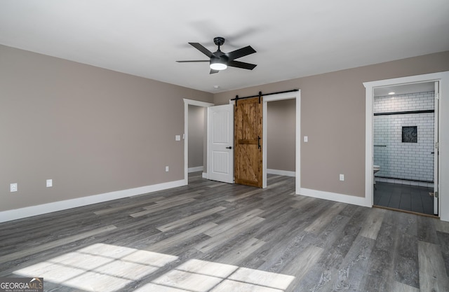 unfurnished bedroom featuring a barn door, ensuite bathroom, ceiling fan, and hardwood / wood-style flooring