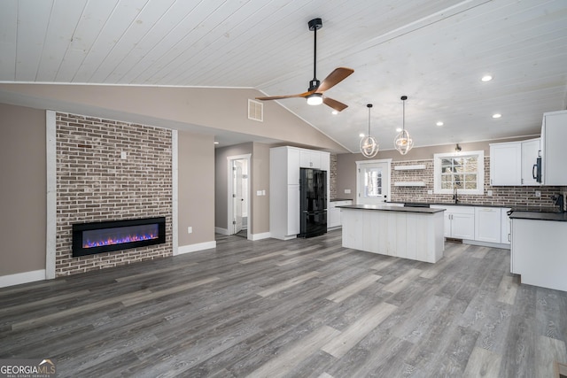 kitchen with dark countertops, open floor plan, freestanding refrigerator, vaulted ceiling, and a sink