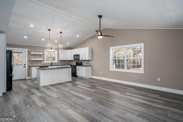 kitchen with black appliances, a healthy amount of sunlight, white cabinets, and lofted ceiling