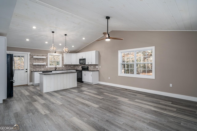 kitchen featuring wood finished floors, a center island, lofted ceiling, dark countertops, and black appliances