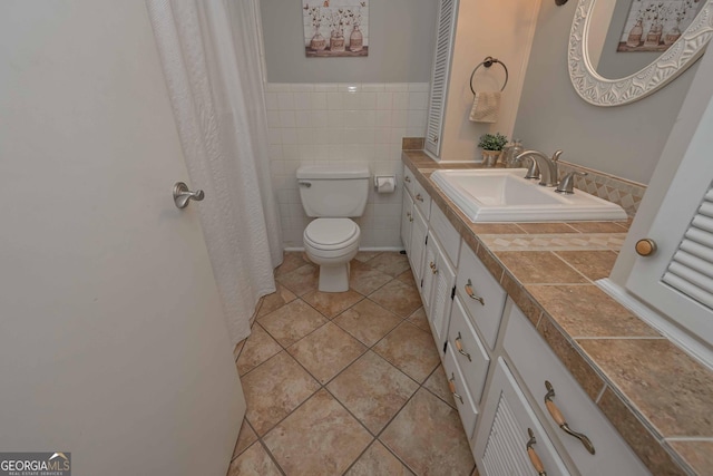 bathroom with toilet, vanity, tile patterned floors, and tile walls