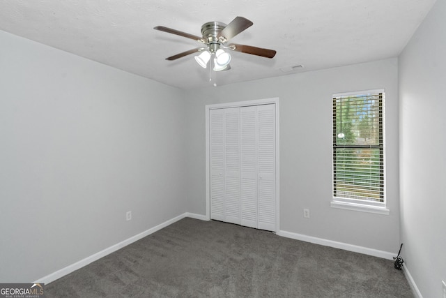 unfurnished bedroom with ceiling fan, dark carpet, and a closet